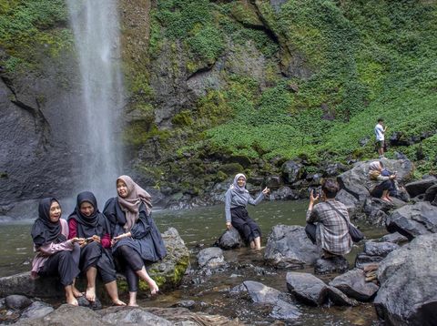 Wisatawan berfoto dengan latar belakang Curug Pelangi Cimahi di Cisarua, Kabupaten Bandung Barat, Jawa Barat, Minggu (27/10/2024). Air terjun atau curug yang memiliki ketinggian 87 meter dan menjadi salah satu air terjun tertinggi di Jawa Barat tersebut berpotensi menjadi destinasi wisata unggulan yang dapat meningkatkan kunjungan pariwisata serta perekonomian masyarakat di kawasan tersebut. ANTARA FOTO/Abdan Syakura/agr