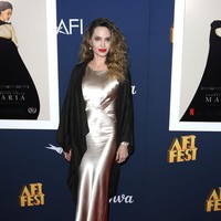 Jolie yang tampil ala Old Hollywood Glam, terlihat elegan dalam balutan gaun sutra berwarna sampanye yang memiliki kerah tinggi dan detail dart atau lipatan kupnat pada bagian dada. Dia melengkapi penampilannya dengan selendang hitam, anting-anting mutiara dan gelang yang serasi dengan busananya. Foto: Getty Images