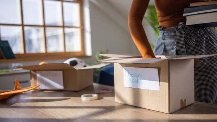 Unrecognizable Caucasian female volunteer, packing books and toys for donation into cardboard box.