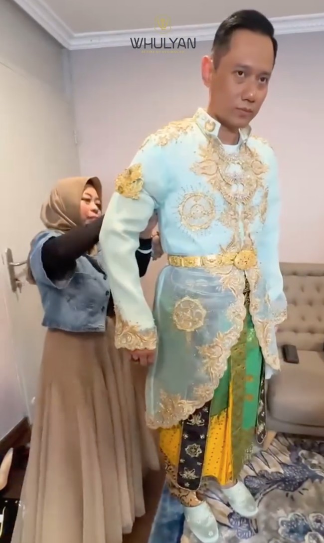 Atasan busana pengantin yang berwarna biru muda itu tampak memiliki ukiran berwarna emas. Atasan lengan panjang tersebut dipadukan dengan kain berwarna hijau dan kuning. Foto: Instagram/@barry_irawan/@whulyan