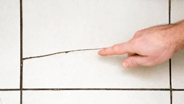 Mans hand finger pointing to the cracked tile on the floor. Building problems and solutions concept.