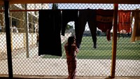 Seorang anak tengah melihat anak lainnya bermain sepakbola.  