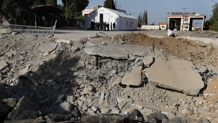 Potret Kondisi Perbatasan Suriah-Lebanon Pascaserangan Israel People gather near a crater caused by an Israeli airstrike, which blocks the road between the Lebanese and the Syrian crossing points, in Jousieh, Syria, Sunday, Oct. 27, 2024. (AP Photo/Omar Sanadiki)