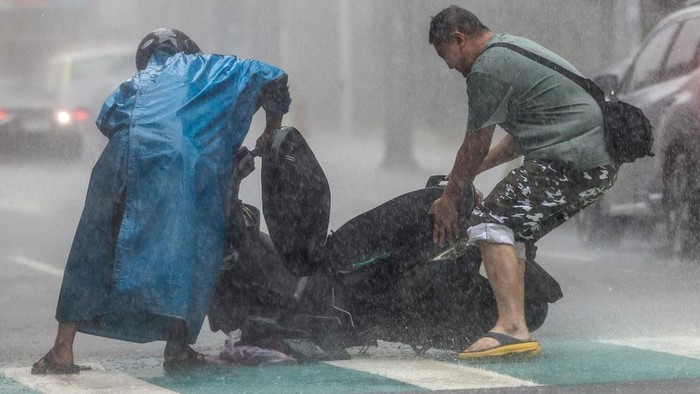A man (R) helps a motorist with a scooter amid heavy rain due to Super Typhoon Kong-rey in Keelung on October 31, 2024. Taiwan shut down on October 31 as Super Typhoon Kong-rey neared, forcing thousands to flee from one of the most powerful storms to threaten the island in years. (Photo by I-Hwa CHENG / AFP)