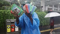 Pedagang jas hujan menawarkan jas hujan plastik untuk warga.