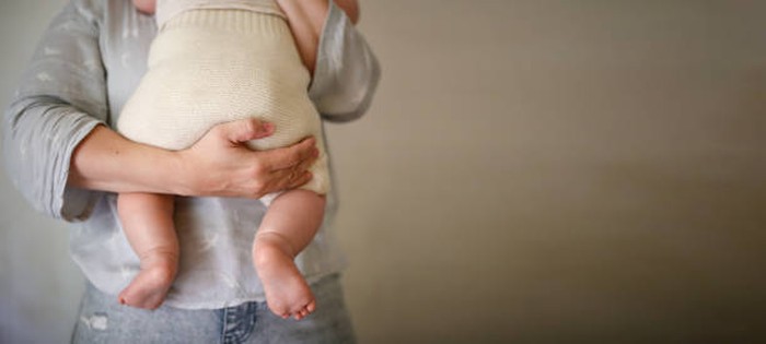 mother holds her baby in eco-friendly diaper, conscious consumption and motherhood, eco-friendly swaddling systems and replacement of disposable diapers, faceless and close up