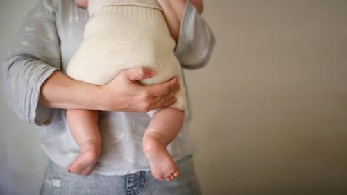 mother holds her baby in eco-friendly diaper, conscious consumption and motherhood, eco-friendly swaddling systems and replacement of disposable diapers, faceless and close up