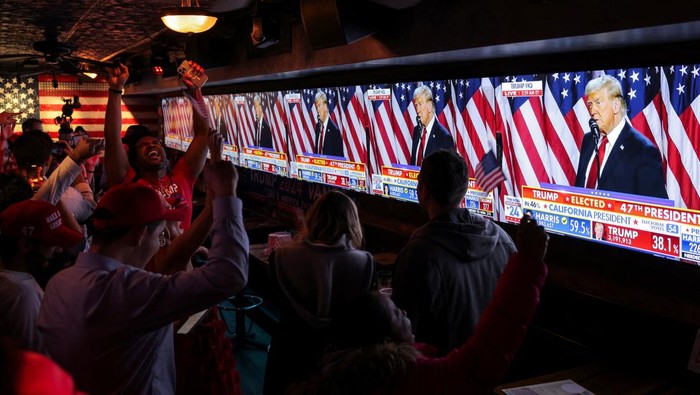 Supporters of Republican presidential nominee former U.S. President Donald Trump react next to screens showing Trump speak from the Palm Beach County Convention Center, as they attend the New York Young Republican Club watch party during the 2024 U.S. presidential election, in Manhattan, New York City, U.S., November 6, 2024. REUTERS/Andrew Kelly