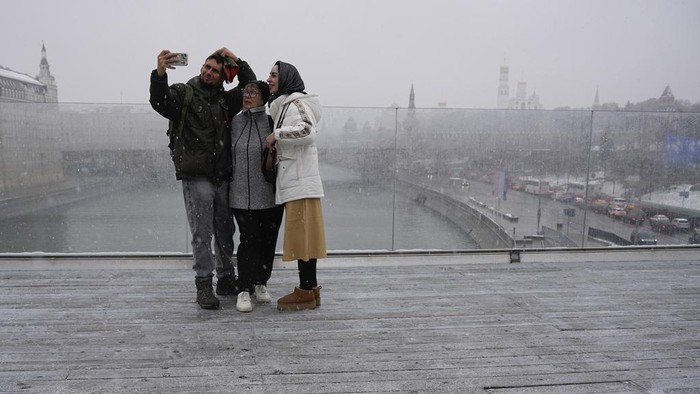 A man walks at Zaryadye park with the Spasskaya tower of the Kremlin and St. Basil's Cathedral in the background during a snowfall in Moscow, Russia, Wednesday, Nov. 6, 2024. (AP Photo/Pavel Bednyakov)