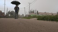 Warga melintas menggunakan payung saat hujan abu dan pasir vulkanis dari erupsi Gunung Lewotobi Laki-laki di Desa Pululera. 