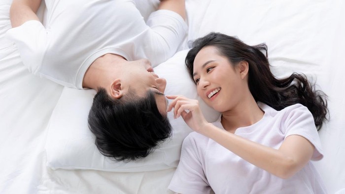 Happy Asian couple lying down smiling and relaxing together in bed.