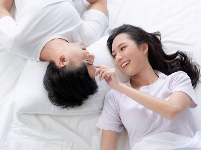 Happy Asian couple lying down smiling and relaxing together in bed.