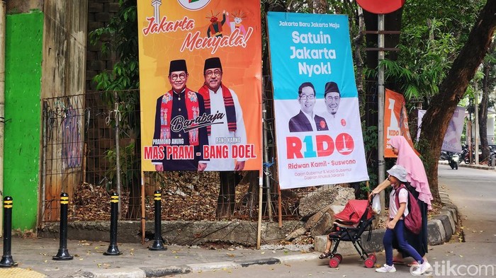 Warga melintas di dekat Alat Peraga Kampanye (APK) yang terpasang di sejumlah tempat di Jakarta, Jumat (8/11/2024). Pada bulan kedua masa kampanye Pilkada Jakarta, spanduk mulai bertebaran di tempat umum. Foto, program dan janji manis paslon dijadikan bahan utama APK. Spanduk APK dipasang pada tempat yang diperbolehkan, sebagian tidak sesuai dengan Peraturan Komisi Pemilihan Umum (PKPU) Tentang Kampanye Pemilihan Gubernur dan Wakil Gubernur seperti dipaku di pohon.