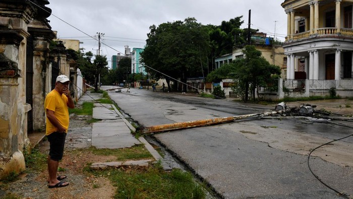 People stand by a tree uprooted by heavy winds after Hurricane Rafael knocked out the country's electrical grid, leaving 10 million people without electrical service, in Havana, Cuba, November 7, 2024. REUTERS/Norlys Perez     TPX IMAGES OF THE DAY