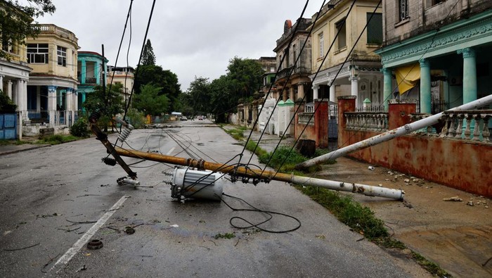 People stand by a tree uprooted by heavy winds after Hurricane Rafael knocked out the country's electrical grid, leaving 10 million people without electrical service, in Havana, Cuba, November 7, 2024. REUTERS/Norlys Perez     TPX IMAGES OF THE DAY