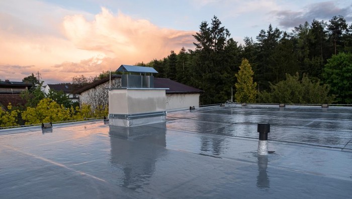 Flat roof covered with bitumen membrane and silver lacquer with chimney on a private house. Reflections after rain