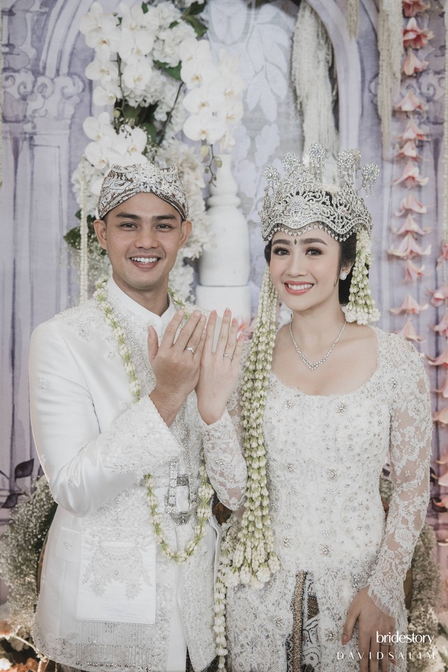 Kebaya putih klasik yang dikenakan Febby merupakan rancangan dari desainer Vera Kebaya. Kebaya brukat tersebut dipadukan dengan kain lilit berwarna coklat. Foto: Bridestory