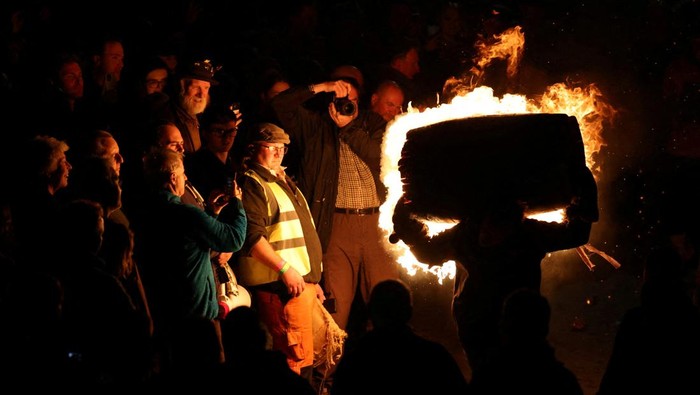 Melihat Keseruan Tradisi Mengangkat Tong Berapi di Inggris A teenager carrying a flaming tar barrel runs through the street in Ottery St. Mary on Guy Fawkes night in Britain, November 5, 2024. REUTERS/Hollie Adams