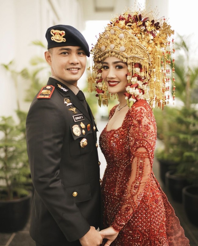 Dalam resepsi pernikahannya, Febby tampil memukau dengan baju pengantin Palembang berwarna merah menyala yang dirancang khusus oleh Studio Boh. Sedangkan suaminya Ajat memakai seragam lengkap dengan atribut polisi, yang dirancang oleh Wong Hang Tailor. Foto: dok. Instagram @morden.co, dok. Instagram @marlenehariman