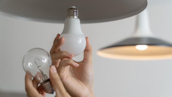 A young woman is changing a light bulb from an incandescent bulb to an LED bulb.