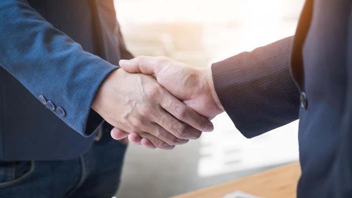 Dua orang berjabat tangan yang menandai persetujuan atau kerja sama bisnis