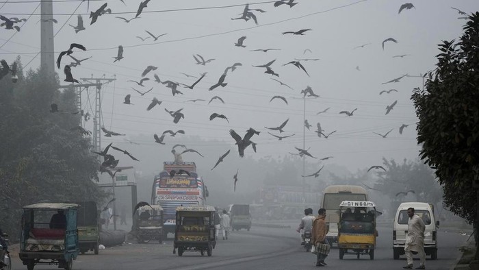 People cross a road as smog envelopes the areas of Lahore, Pakistan, Wednesday, Nov. 13, 2024. (AP Photo/K.M. Chaudary)