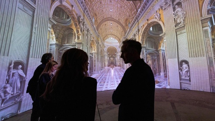 Vatikan Luncurkan Tur Virtual Berbasis AI untuk Basilika Santo Petrus Visitors look at AI-generated images of St. Peter's Basilica as the Vatican presents a new AI-enhanced experience developed in collaboration with Microsoft for tourists visiting the Basilica at the Vatican, November 9, 2024. REUTERS/Remo Casilli