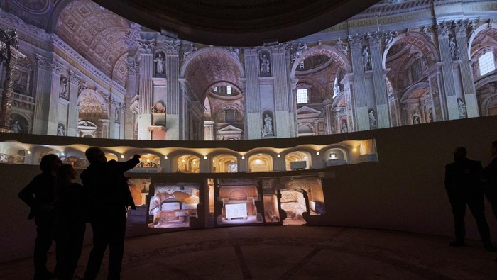 Vatikan Luncurkan Tur Virtual Berbasis AI untuk Basilika Santo Petrus Visitors look at AI-generated images of St. Peter's Basilica as the Vatican presents a new AI-enhanced experience developed in collaboration with Microsoft for tourists visiting the Basilica at the Vatican, November 9, 2024. REUTERS/Remo Casilli