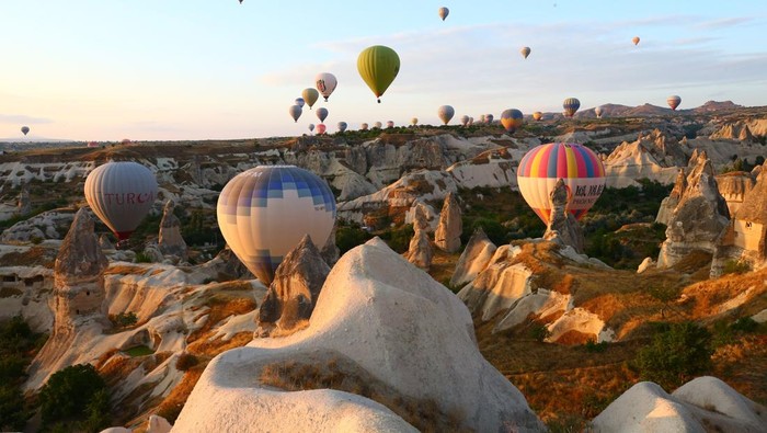 NEVSEHIR, TURKEY - AUGUST 10: Hot air balloons glide over historical Cappadocia region, located in Nevsehir province of Turkey  on August 10, 2021.  A total of 138,225 tourists enjoyed hot air balloon tours in Turkeyâs charming touristic hub Cappadocia between January and July. Cappadocia, listed as one of the UNESCO World Heritage places, is famous with its distinctive plateau, valleys, hills, unique fairy chimney volcanic cones, colorful frescos covering underground cities, boutique hotels, houses carved into rocks, rock churches, chapels, and shelters used by early Christians. (Photo by Behcet Alkan/Anadolu Agency via Getty Images)