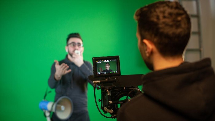 Camera man films guy with speaker on camera with green screen background