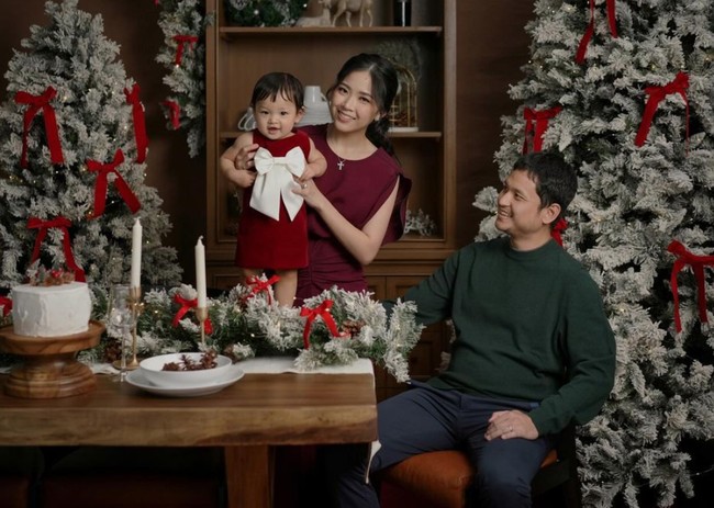 Mengenakan busana dengan tema warna Natal, merah dan hijau, Jessica dan keluarga tampil menawan. Jessica memilih dress warna burgundy dengan riasan natural dan rambut yang diikat ke belakang. Baby Julia yang digendongnya tampil dengan dress merah tua yang memiliki aksen pita warna putuh cukup besar pada bagian depannya. Foto: Instagram/@juniapics
