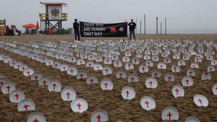People hold a banner at Copacabana beach, as activists from NGO Rio de Paz display 733 empty plates with red crosses, representing the 733 million people who suffer from hunger worldwide, ahead of the G20 summit in Rio de Janeiro, Brazil November 16, 2024. REUTERS/Pilar Olivares
