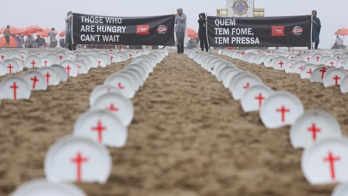People hold a banner at Copacabana beach, as activists from NGO Rio de Paz display 733 empty plates with red crosses, representing the 733 million people who suffer from hunger worldwide, ahead of the G20 summit in Rio de Janeiro, Brazil November 16, 2024. REUTERS/Pilar Olivares