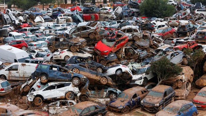 Women walk past a site where cars damaged by heavy rains have piled up in Catarroja, Valencia, Spain, November 16,2024. REUTERS/Eva Manez
