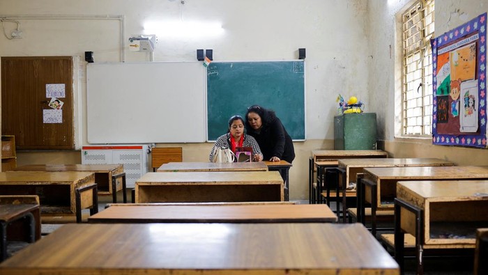 School teachers conduct online classes using a mobile phone in an empty classroom after schools were ordered shut by the Delhi government as Delhi's air quality worsened due to air pollution, on a smoggy morning in New Delhi, India, November 19, 2024. REUTERS/Anushree Fadnavis