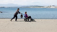 Suami dari ahli manikur Jepang Naomi Arimoto mendorongnya di kursi roda saat ia mengumpulkan sampah plastik dari pasir di sebuah pantai di Chigasaki, Prefektur Kanagawa, Jepang, 21 Oktober 2024.  
