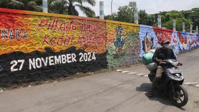 Warga melintasi mural sosialisasi penyelenggaraan Pilkada 2024 di Kediri Jawa Timur, Rabu (20/11/2024). Komisi Pemilihan Umum (KPU) Kabupaten Kediri bekerja sama dengan komunitas seniman membuat mural di sejumlah titik strategis sebagai upaya sosialisasi penyelenggaraan Pilkada 2024 guna mendongkrak partisipasi masyarakat menggunakan hak pilihnya pada 27 November 2024 mendatang. ANTARA FOTO/Prasetia Fauzani/rwa.