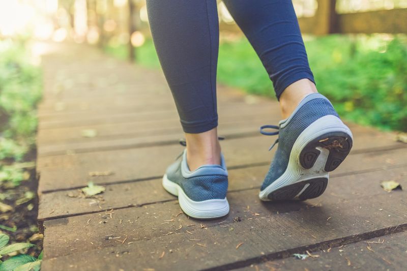 Close up of female legs with running shoes on wooden footpath in woods. Nature and sport healthy lifestyle concept.