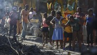 Seorang perempuan merekam adegan di mana jasad para tersangka anggota geng yang dibakar warga tergeletak di tengah jalan, di lingkungan Pétion-Ville, Port-au-Prince, Haiti, Selasa (19/11/2024). (AP Photo/Odelyn Joseph)