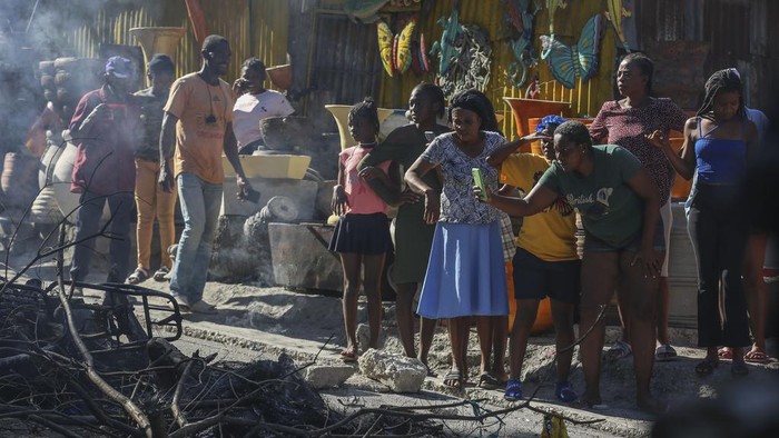 A woman films a scene where the bodies of suspected gang members who were set on fire by residents sit in a heap in the middle of a road, in the Pétion-Ville neighborhood of Port-au-Prince, Haiti, Tuesday, Nov. 19, 2024. (AP Photo/Odelyn Joseph)