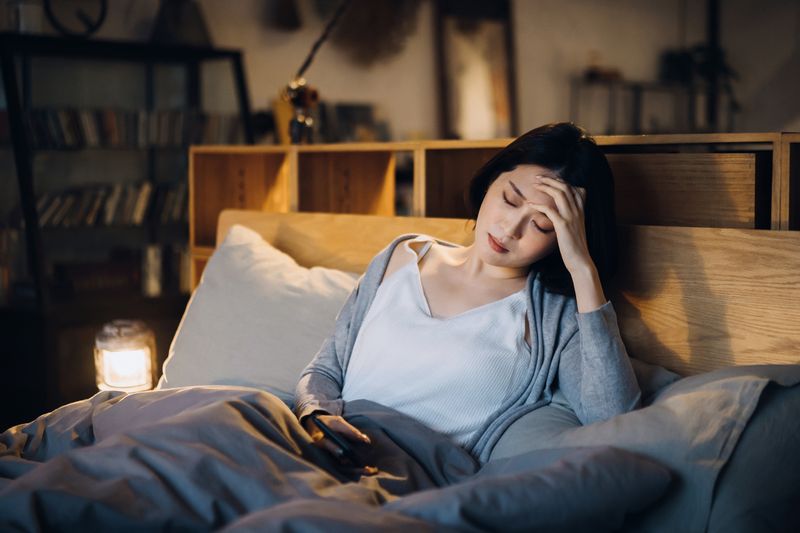 Young Asian woman feeling sick and suffering from a headache, lying on the bed and taking a rest at home