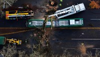Pemandangan drone yang memperlihatkan kru yang bekerja untuk menyingkirkan pohon tumbang yang menimpa sebuah bus.