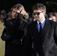 Niall Horan ditemani kekasihnya, Amelia Woolley, berbusana hitam-hitam. Dia mengenakan mantel di atas kemeja putih dan dasi hitam. Raut kesedihan juga terpampang jelas di wajahnya. Foto: AP/Andrew Matthews