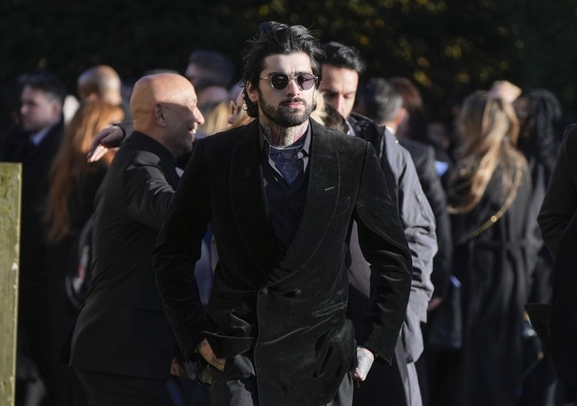 Zayn Malik tampak mengenakan jas hitam beludru dipadu kemeja motif. Penyanyi 31 tahun ini menampakkan raut wajah yang sangat berduka di balik kacamata hitamnya. Foto: AP/Andrew Matthews