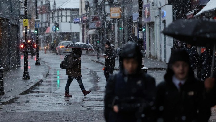 Potret Badai Salju Menghantam Inggris A pedestrian shelters under an umbrella while walking during the first snow fall of the season in Rickmansworth, Britain November 19, 2024. REUTERS/Suzanne Plunkett