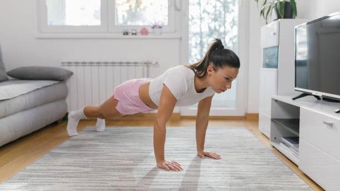 Beautiful young woman in sports clothing doing push-ups at home