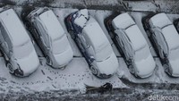 Seorang pekerja membersihkan jalan yang dipenuhi mobil-mobil yang tertutup salju di tengah hujan salju pertama di Kyiv, Ukraina.