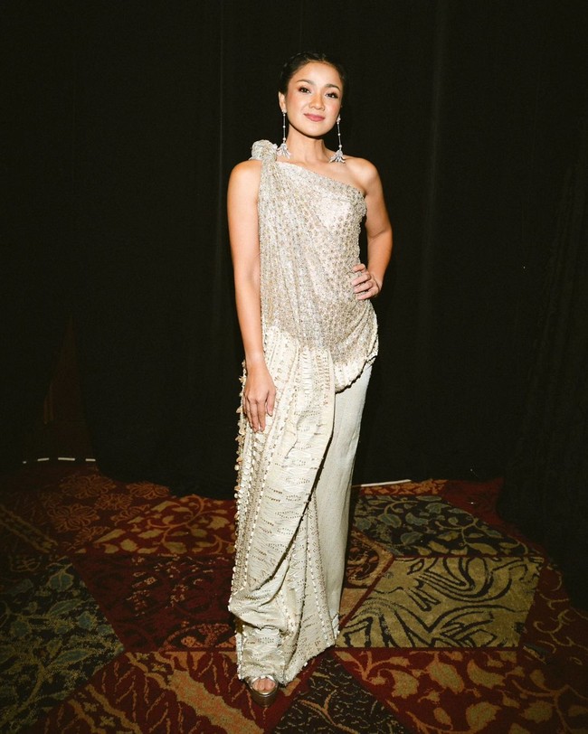 Gaun yang terbuat dari ulos ini memiliki potongan asimetris denhan aksen drapery yang cantik. Tebaran payet dan bordir emas membuat penampilannya berkilau. Foto: Instagram/@hagaipakan @agrasuseno