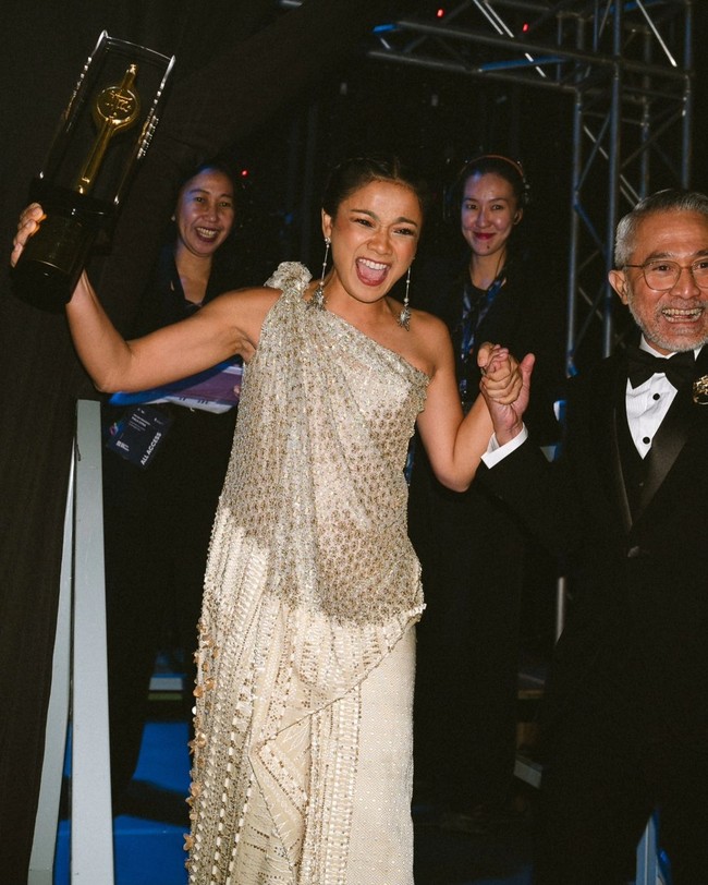 Menerima Piala Citra untuk kedua kalinya, presenter sekaligus aktris ini cantik dan elegan dalam balutan gaun one-shoulder rancangan Biyan Wanaatmadja. Foto: Instagram/@hagaipakan @agrasuseno