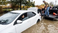Sejumlah warga berusaha mengevakuasi mobil yang mogok akibat menerobos banjir. AP Photo/Noah Berger. 